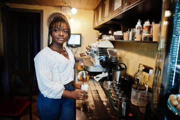 Stylish african american women in white blouse and blue jeans posed at cafe with caramel latte.