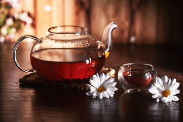 Glass teapot with tea on a dark background with flowers