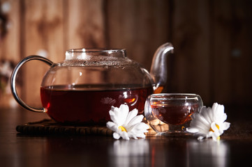 Teapot with tea on a dark background with flowers