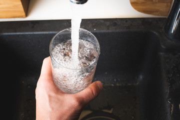 Filling glass of water from stainless steel kitchen faucet. Drinking water concept
