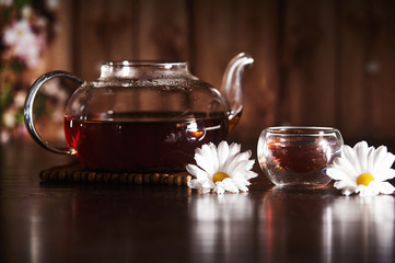 Teapot with tea on a dark background with flowers