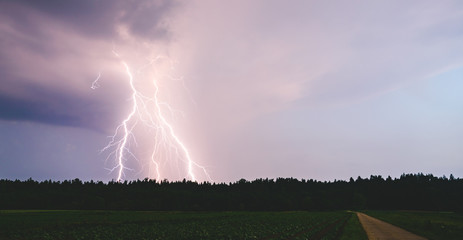 Dramatic lightning bolt at night over rural area. Agriculture fields.