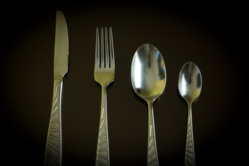 Still life of the kitchen objects. Silver knife, fork, spoon, teaspoon on the dark reflective backdrop.
