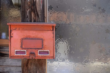Old red metal mailbox hanging on wall.