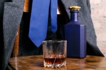 Closeup of glass of alcoholic drink, blue bottle on the wooden chair, man`s cloth on the chair.Concept of relax in the bar