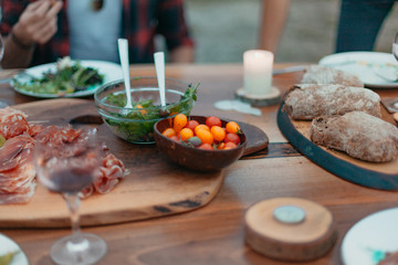 Friends and family gathered for picnic dinner for Thanksgiving. Festive young people celebrating life with red wine, grapes, cheese platter, and a selection of cold meats