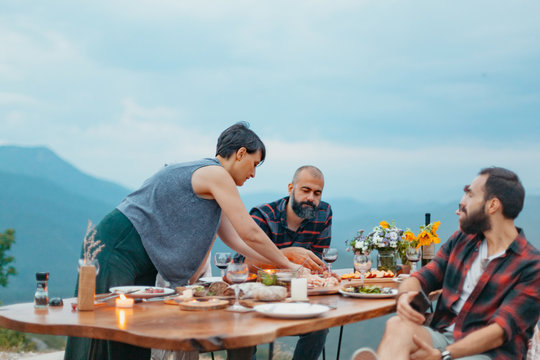 Friends and family gathered for picnic dinner for Thanksgiving. Festive young people celebrating life with red wine, grapes, cheese platter, and a selection of cold meats
