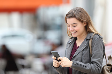 Happy teen texting on cell phone walking in the street
