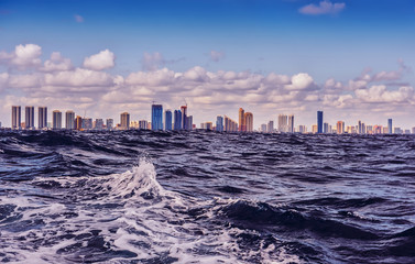   View of skyscrapers away from the ocean. Waves in the foreground and city silhouettes on the horizon. USA. Florida. Miami