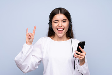 Fototapeta premium Young woman over isolated blue background using the mobile with headphones and singing