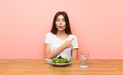 Young woman with a salad surprised and pointing side