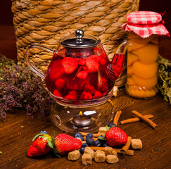  black tea with strawberries in a glass teapot on a dark background