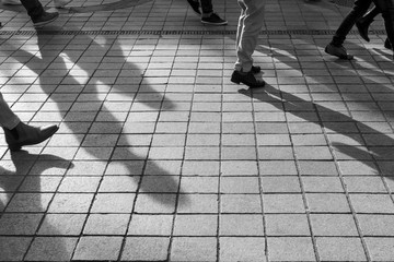 Black and White photo of shadow of people. Pedestrian in a street. Shadow of people walking on the street. Silhouettes and Shadows of a person on the street. Person walking down on sidewalk.
