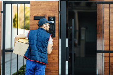 Rear view of a courier ringing on customer's intercom while making home delivery.