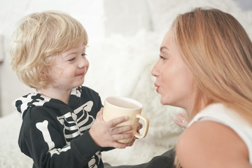 Beautiful little boy enjoying a cup of drink at white home background
