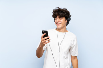 Young man listening music with a mobile over isolated blue wall