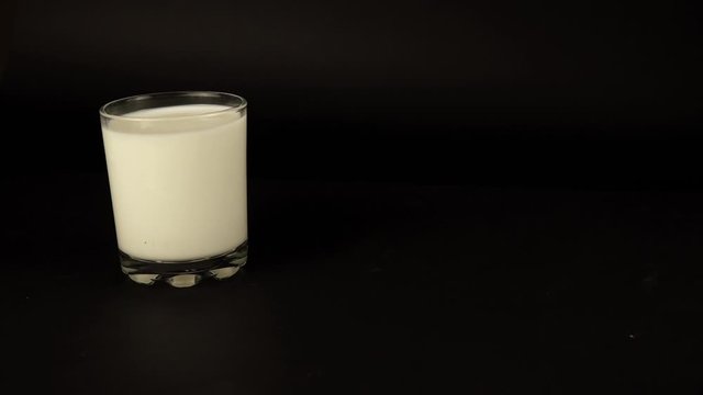 a man's hand puts a glass of milk, yogurt and one banana on a black background