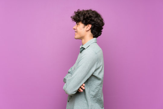 Young man over isolated purple wall in lateral position