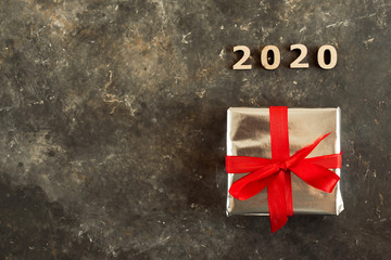 Festive background with a beautiful brightly wrapped gift in shiny paper and a red ribbon with a bow. 2020 laid out with wooden figures, top view
