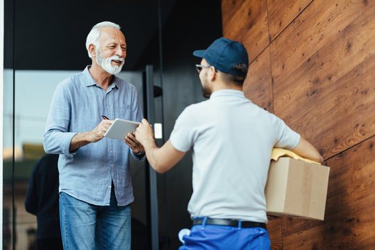 Happy senior man communicating with a courier while signing for delivery on touchpad.