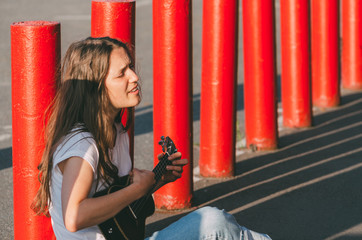 Young woman playing ukulele on the street, near red bollards
