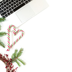 Christmas / New Year holiday composition. Home office desk with laptop, Christmas baubles / balls, fir branches, candy sticks on white background. Flat lay, top view festive business concept.