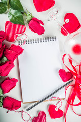 Valentines Day Background with notepad. Love letter Valentines concept notepad, with red roses. red textile hearts and wine glass on white table. Girl hands with pencil writes letter, wishing