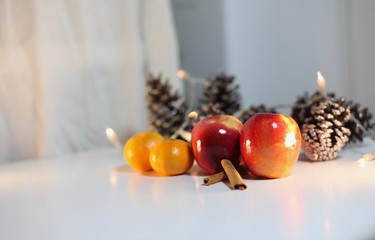 Apples, tangerine and cinnamon on a table with pine cones and Christmas lights