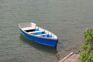 Naklejka na ściany i meble Blue wooden boat was moored to the shore
