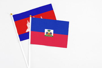 Fototapeta premium Haiti and Cambodia stick flags on white background. High quality fabric, miniature national flag. Peaceful global concept.White floor for copy space.