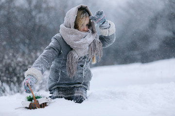 little child girl with a basket goes and looks for the first flowers under the snow in the forest...