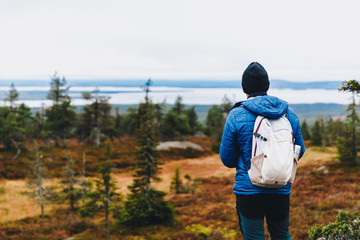 Man traveler in a blue jacket with a backpack hiking in the autumn forest in Finland.