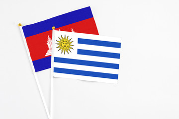 Uruguay and Cambodia stick flags on white background. High quality fabric, miniature national flag. Peaceful global concept.White floor for copy space.