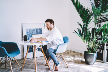 Concentrated young man sitting near table with modern laptop and creating new application with...