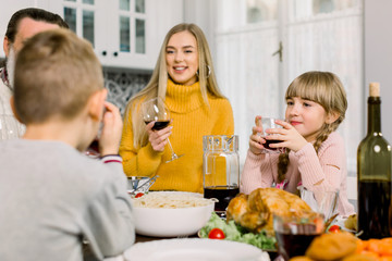 Obraz na płótnie Canvas happy young mother and cute little daughter holding glasses with drinks at thanksgiving holiday table. Family dinner, mother with children boy and girl, grandfather at the table