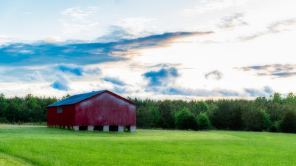 Fototapeta na wymiar Red barn in a field with sky and clouds in the background