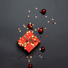 Christmas decorative composition with red paper gift box and gold ribbon bow on a dark background.