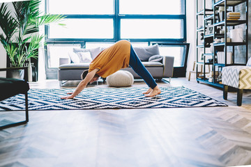 Motivated young man standing in yoga pose on carpet in modern apartment with stylish...