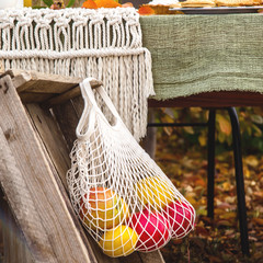 Obraz premium Autumn harvest of apples and pomegranates in a white string bag that hangs on an old rustic box in the garden.