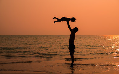 Silhouette picture of asian father and daughter are playing together on the beach in the evening...