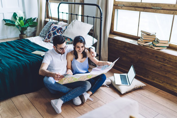 Cheerful couple sitting with paper map and laptop