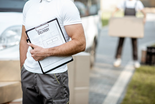 Delivery man with chek list near the car and parcels outdoors, close-up on a clipboard