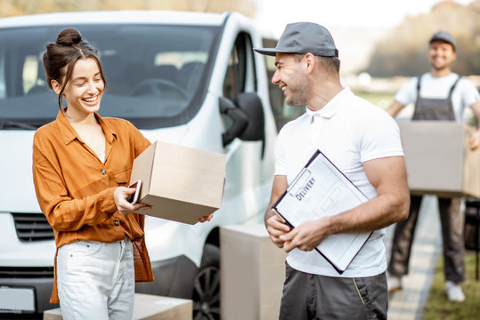 Courier with checklist delivering goods to a young woman by cargo van vehicle, mover with cardboard parcels on the background