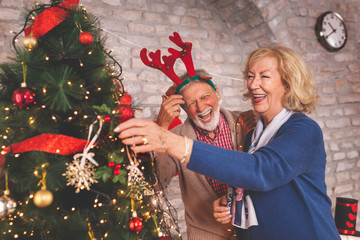 Senior couple having fun while decorating Christmas tree