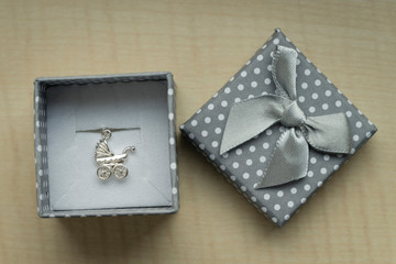 Silver pendant in a box in the shape of a stroller.