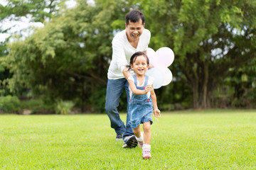 Asian father and daughter are playing the balloons and they running and laughing together with...