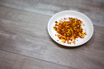 Dried red pepper flakes in a white dish on a wooden background