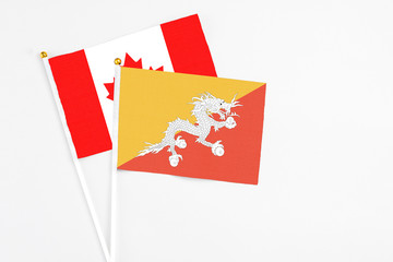 Bhutan and Canada stick flags on white background. High quality fabric, miniature national flag. Peaceful global concept.White floor for copy space.