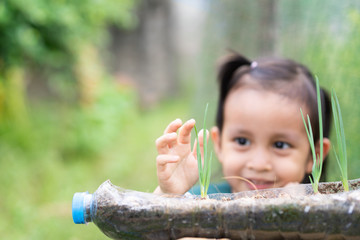 A kindergarten child wear school uniform is holding the plant in the recycle plastic bottle in the green garden background, concep of learning activity for kid and ecology concern of child education.