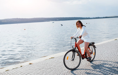 Cheerful girl rides bike on the beach near the lake at sunny daytime